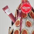 Glass Balm Lip Treatment tube standing upright in Fig Bingsoo, a sheer mauve-nude tinted lip balm, in a teaser shot.
