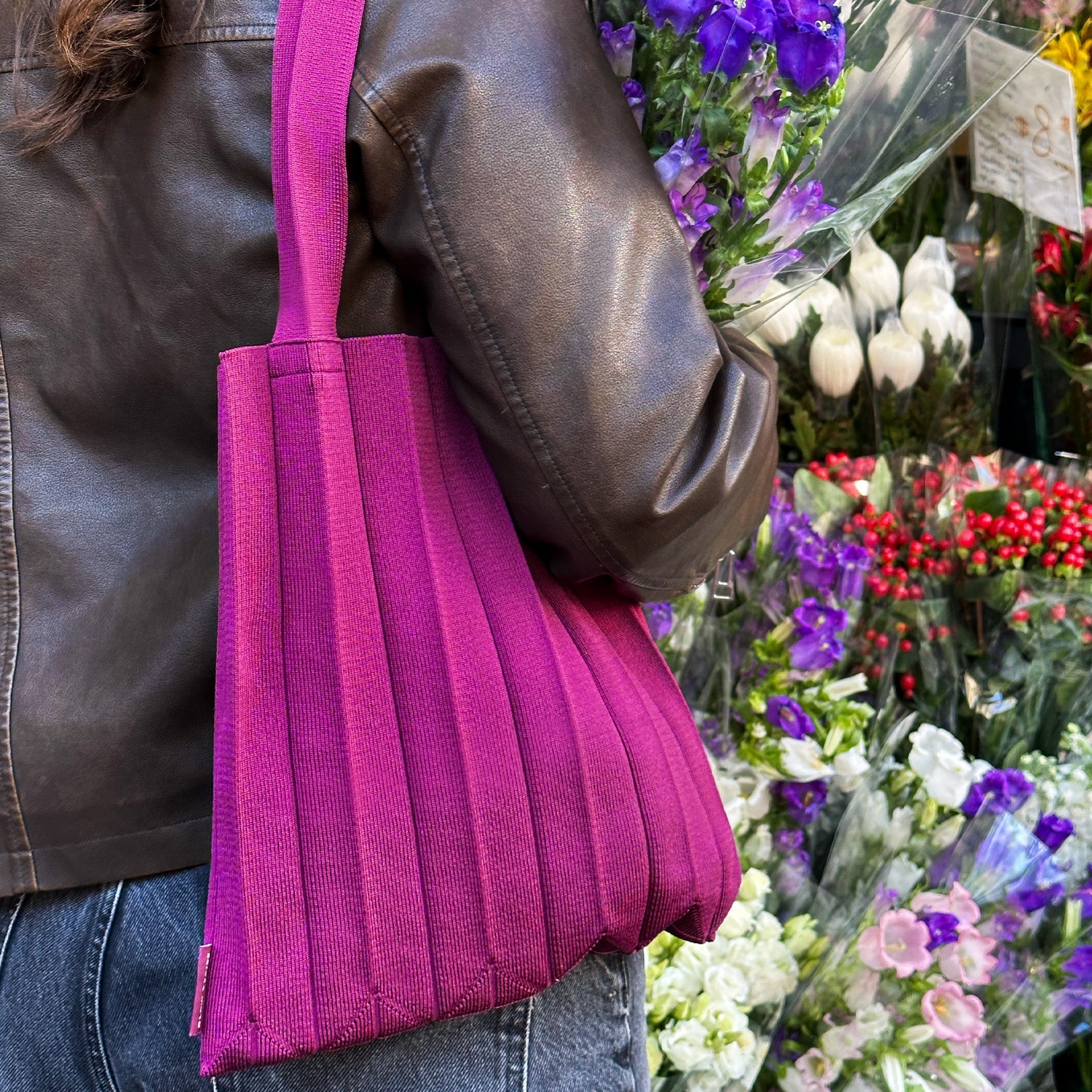 Person holding a pink tote bag with a floral arrangement in the background