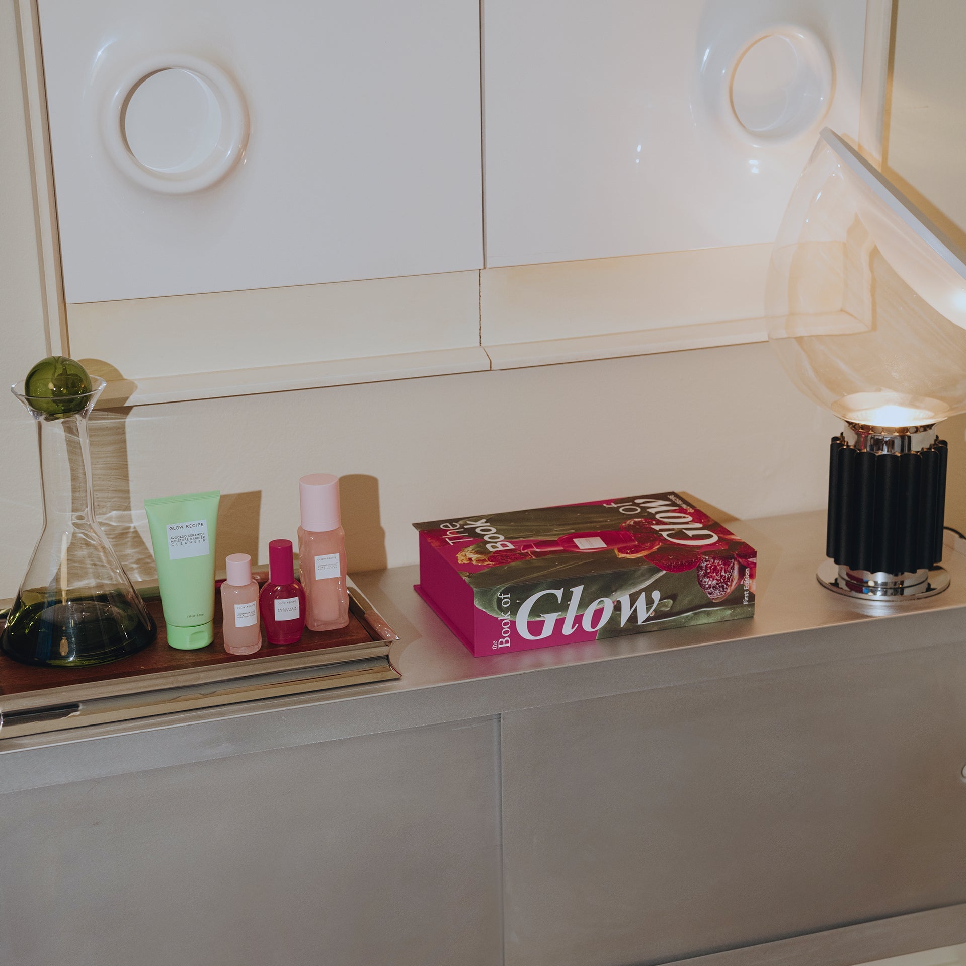 Cosmetic products and a box labeled 'Glow' on a shelf with a neutral background