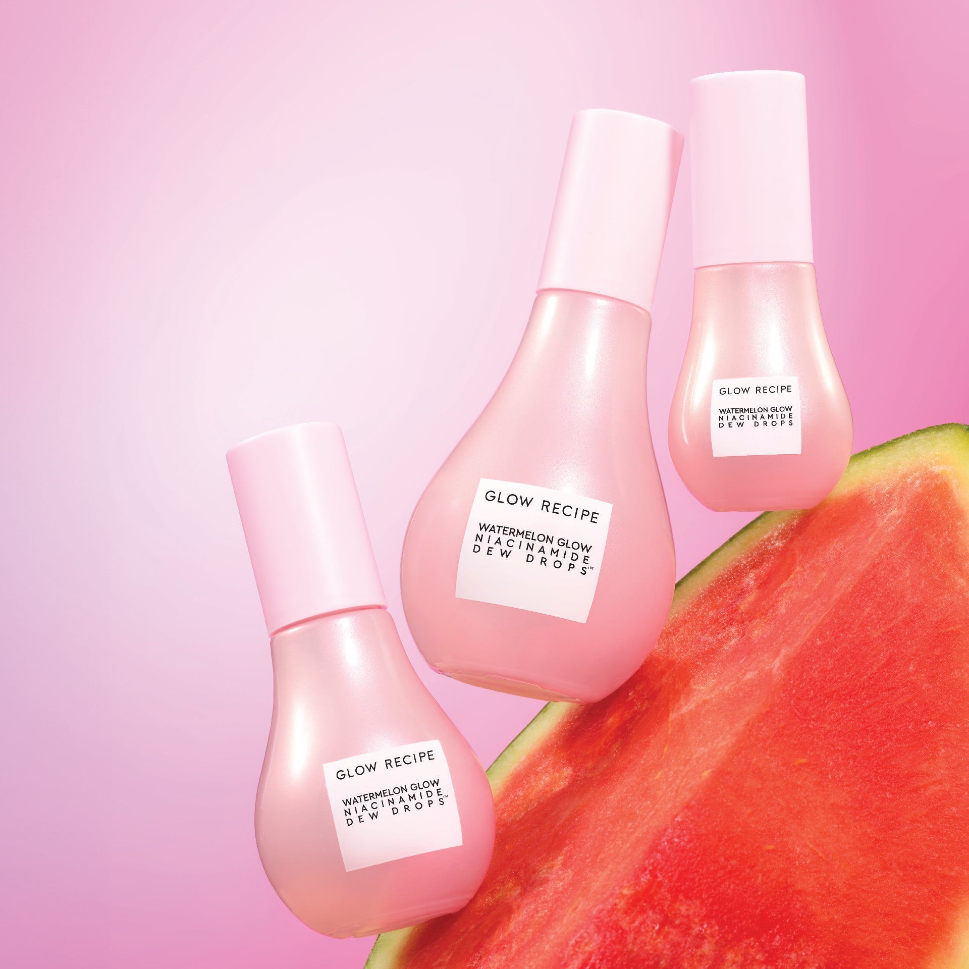 Three sized bottles of Glow Recipe Niacinamide Dew Drop Bottles on watermelon and pink background.