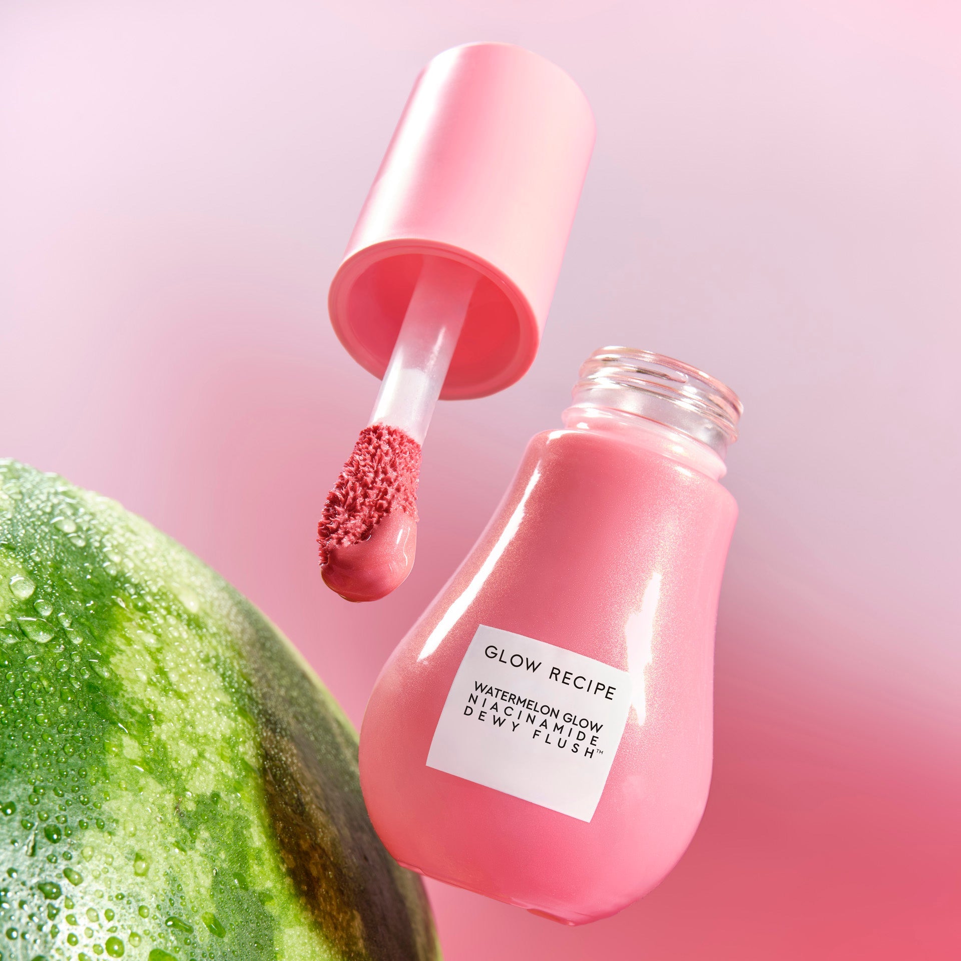 A studio shot of the Dewy Flush bottle in Watermelon Flush is angled to show its soft pink tinted serum.