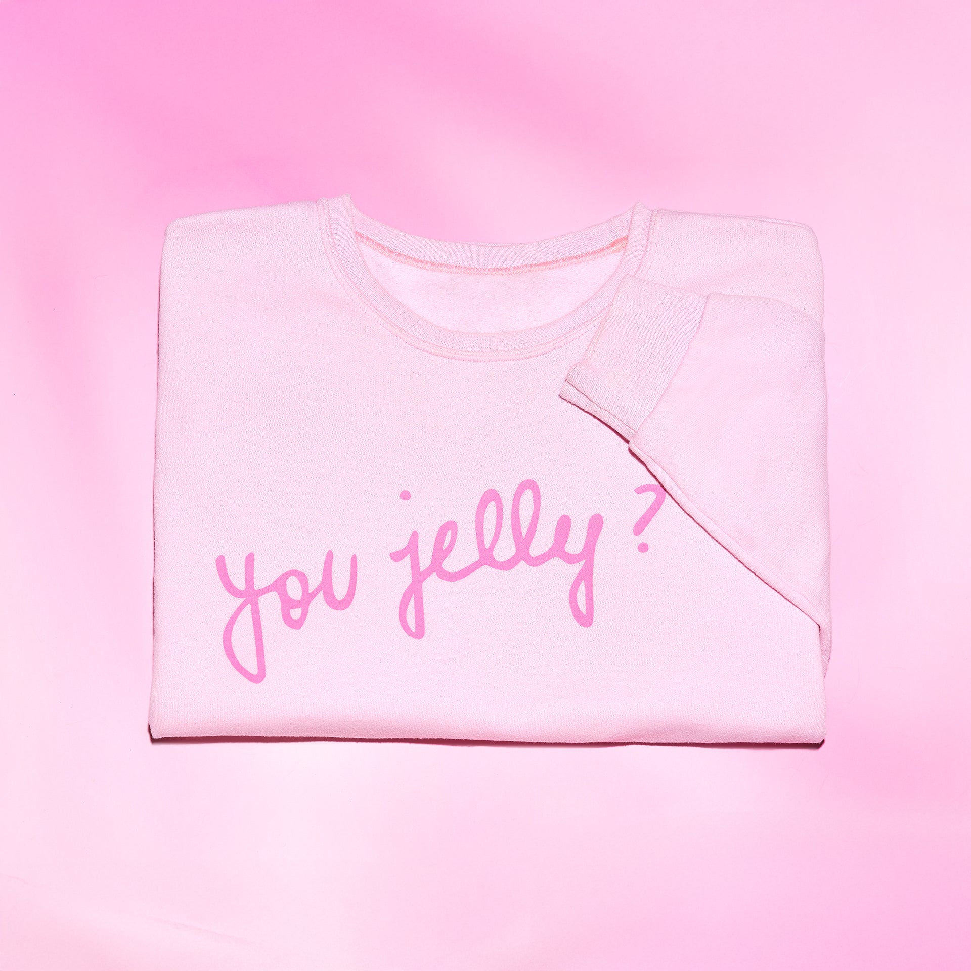 Folded pink sweatshirt with 'you jelly?' text on a pink background