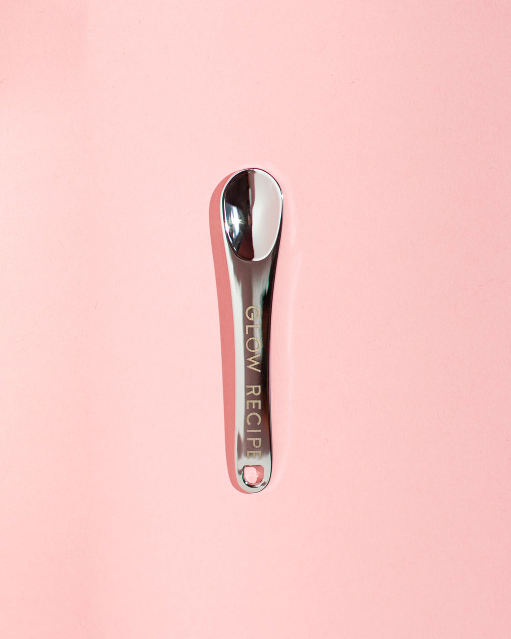 Glow Recipe silver skin care spatula on pink background.