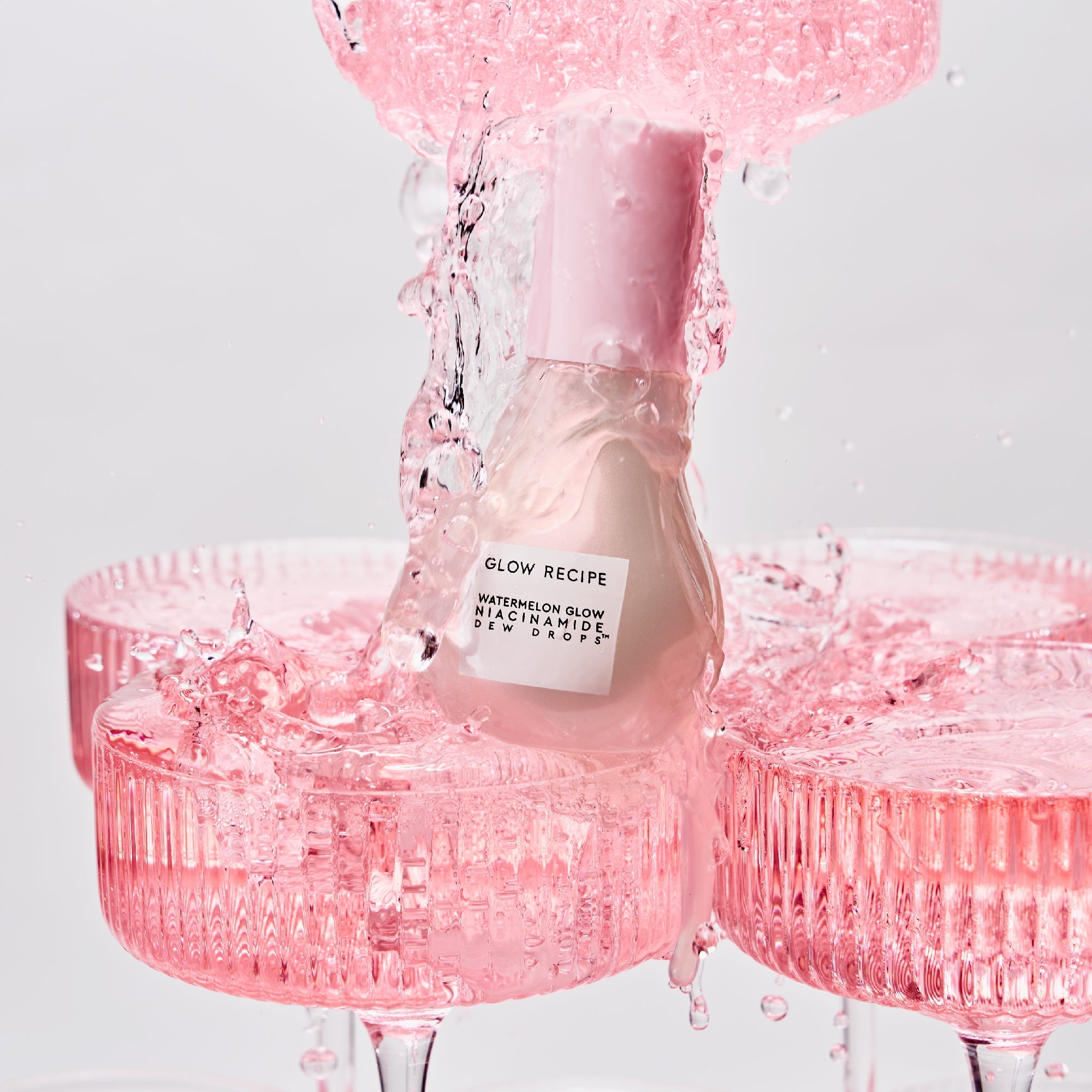 Pink skincare bottle with water droplets on a light gray background