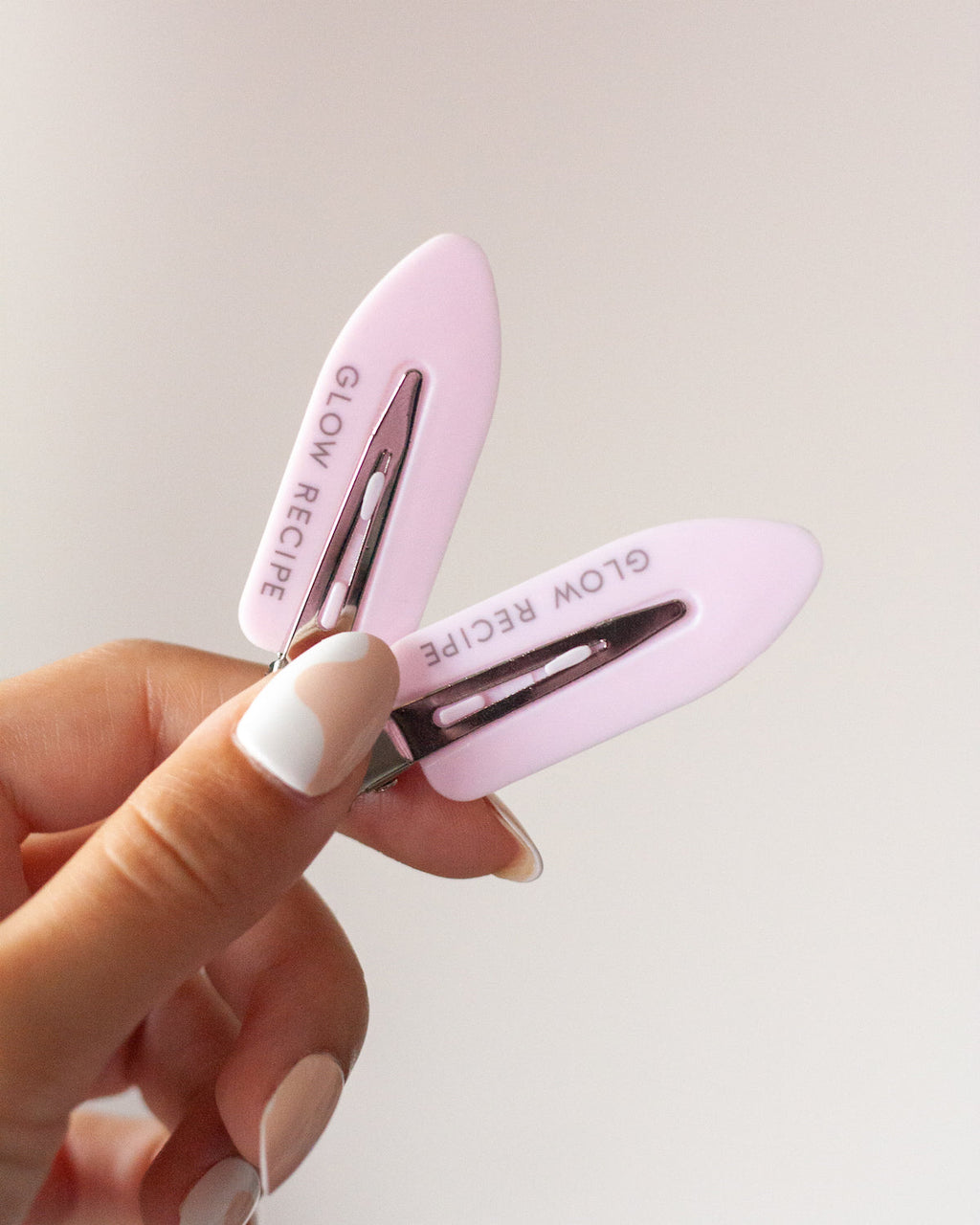 Person holding two Glow Recipe pink clips against beige background.