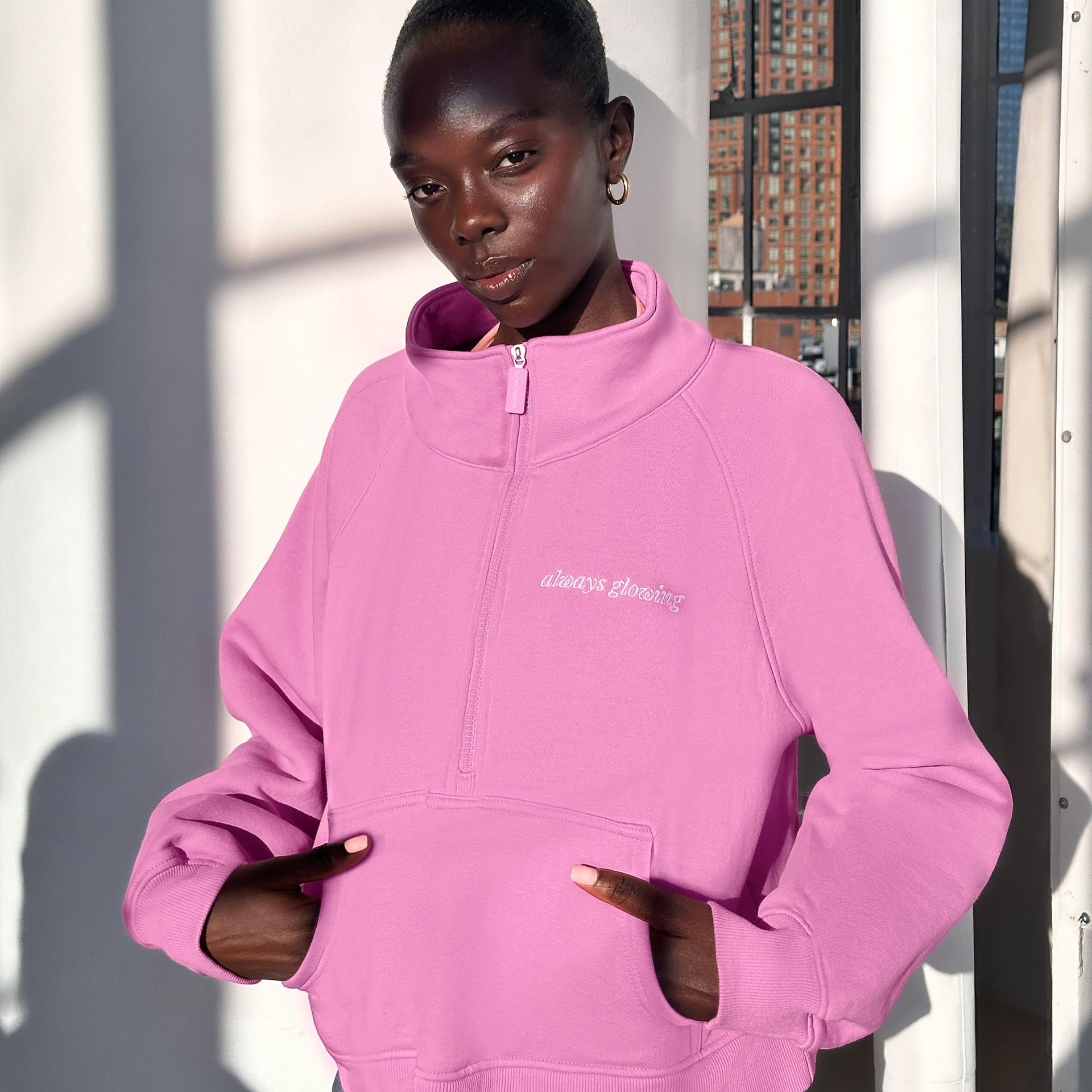 Person wearing a pink hoodie with a brand logo, standing outdoors.