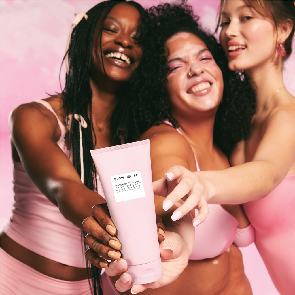 Three women holding a bottle of the Watermelon Glow product. They are wearing pink and standing against a pink background.