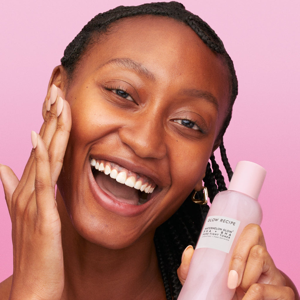 Woman holding a skincare product against a pink background