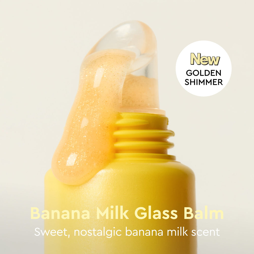 Yellow glass balm with a clear cap on a light gray background, labeled 'New Golden Shimmer Banana Milk Glass Balm'.