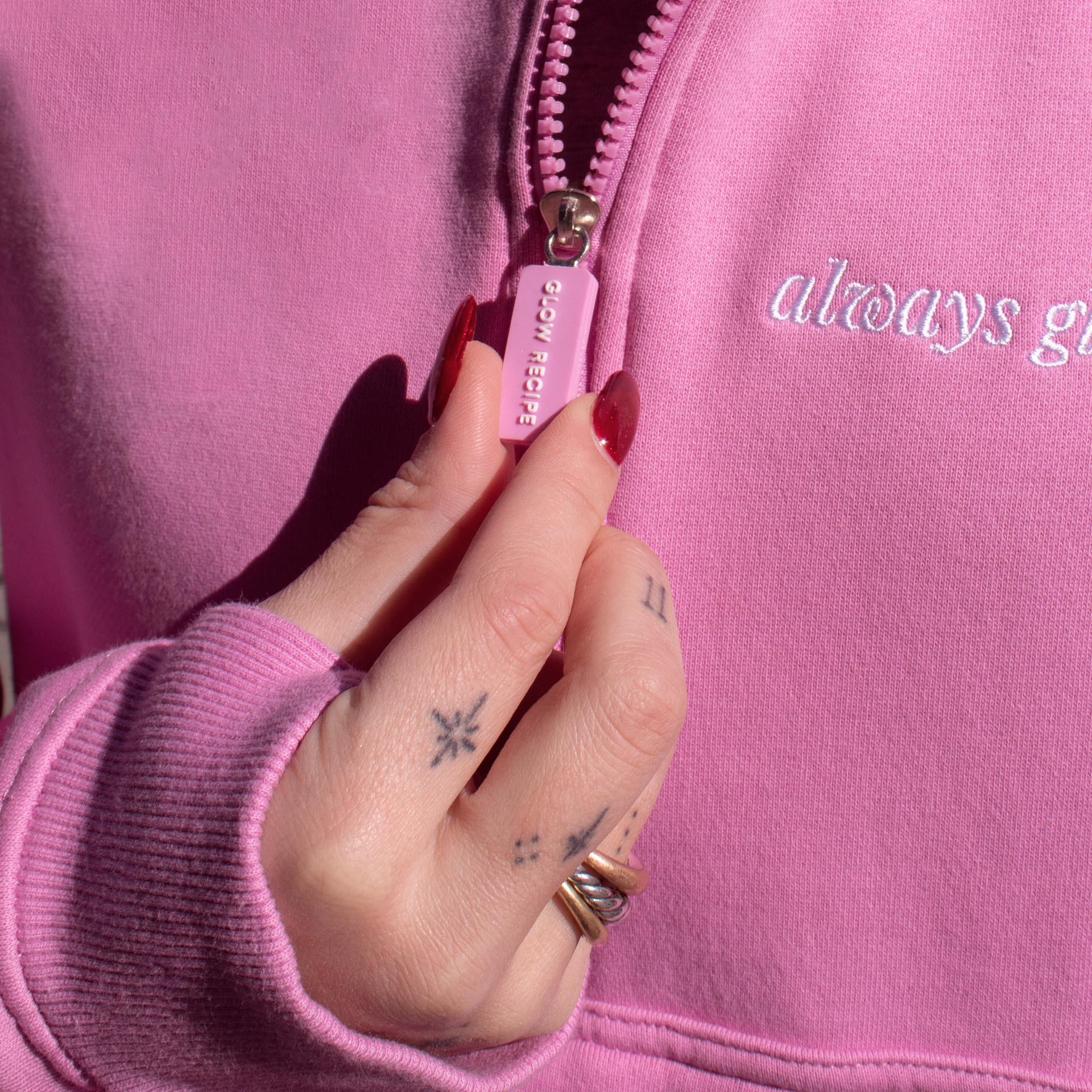 Woman holding the zipper of the pink zip up. The zipper says Glow Recipe.
